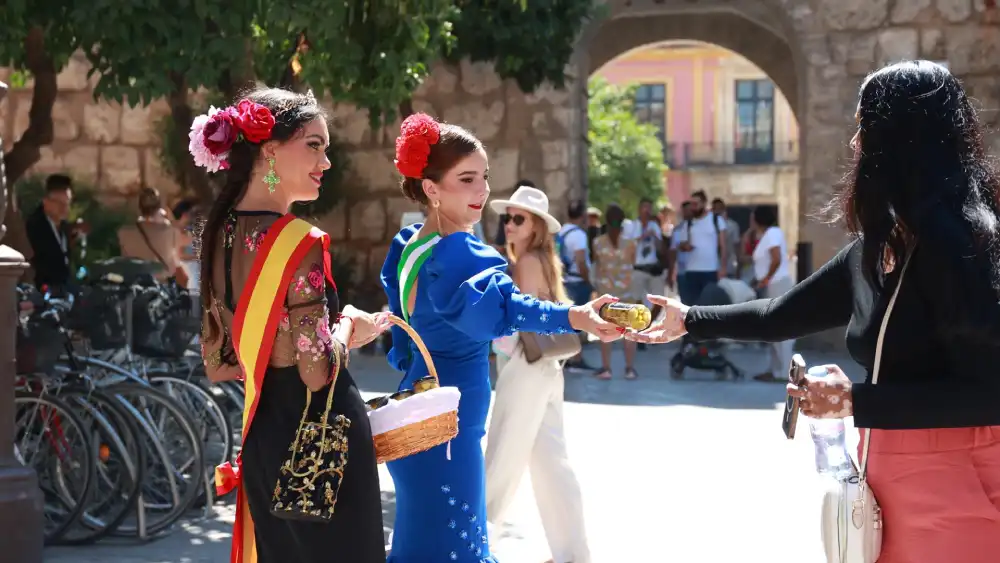 La Reina del Verdeo 2023, Cecilia Ogalla (i), y la dama de Honor y Corte, reparten aceitunas en el centro histórico para la nueva edición de las Fiestas del Verdeo de la localidad de Arahal - ROCÍO RUZ / EUROPA PRESS