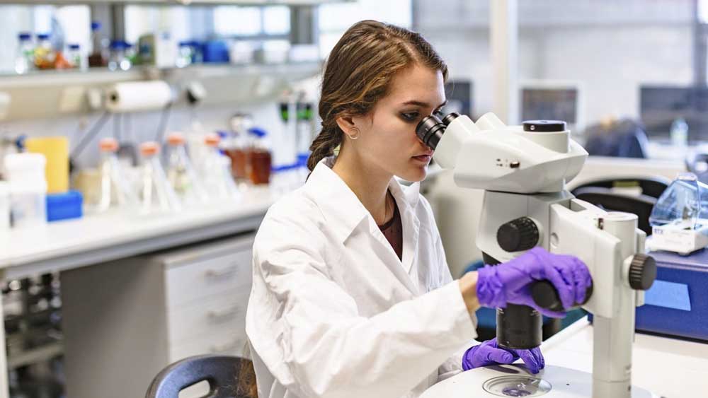 Una científica observa a través de un microscopio. - Paul Gulea