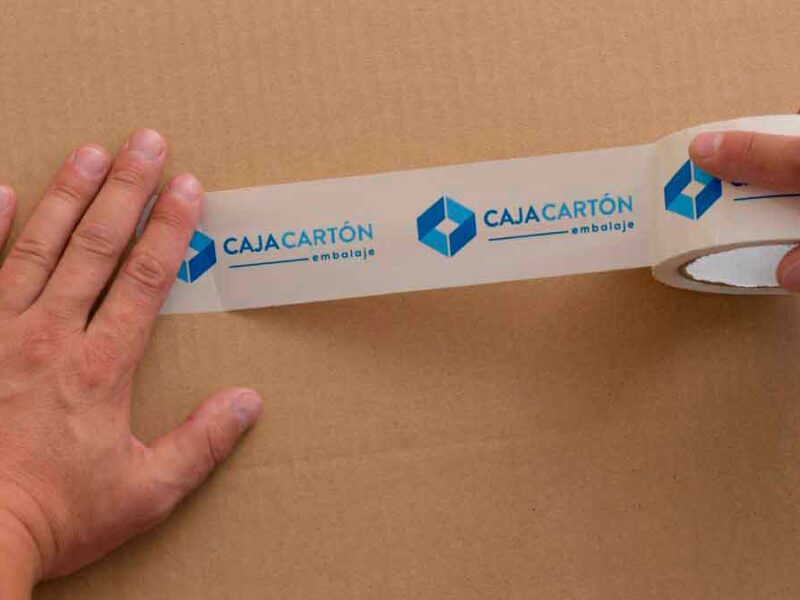 Manos colocando cinta de embalaje personalizada sobre una caja de cartón
