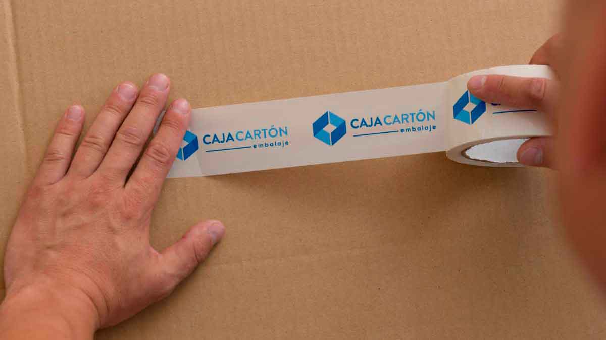 Manos colocando cinta de embalaje personalizada sobre una caja de cartón