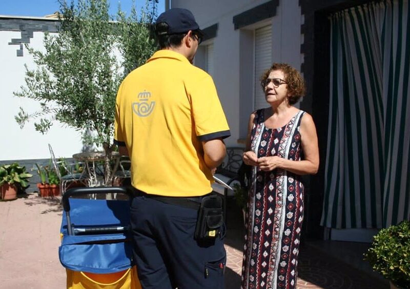 Un cartero rural entrega correspondencia a una vecina de un pueblo. - Correos